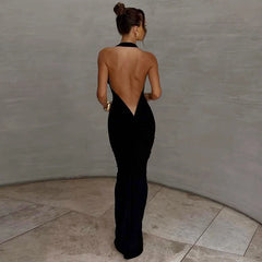 Woman in a black evening gown with an open back standing against a plain wall.