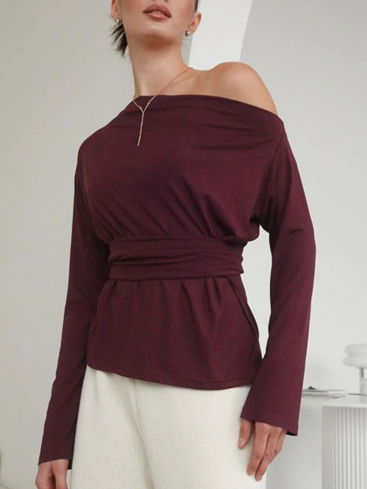 Woman wearing a burgundy off-shoulder top with long sleeves against a white background