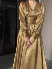 Gold dress with long sleeves and a fitted waist on a neutral background