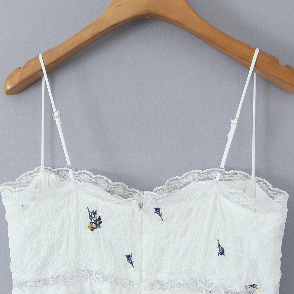White lace top with embroidered details on a wooden hanger against a gray background