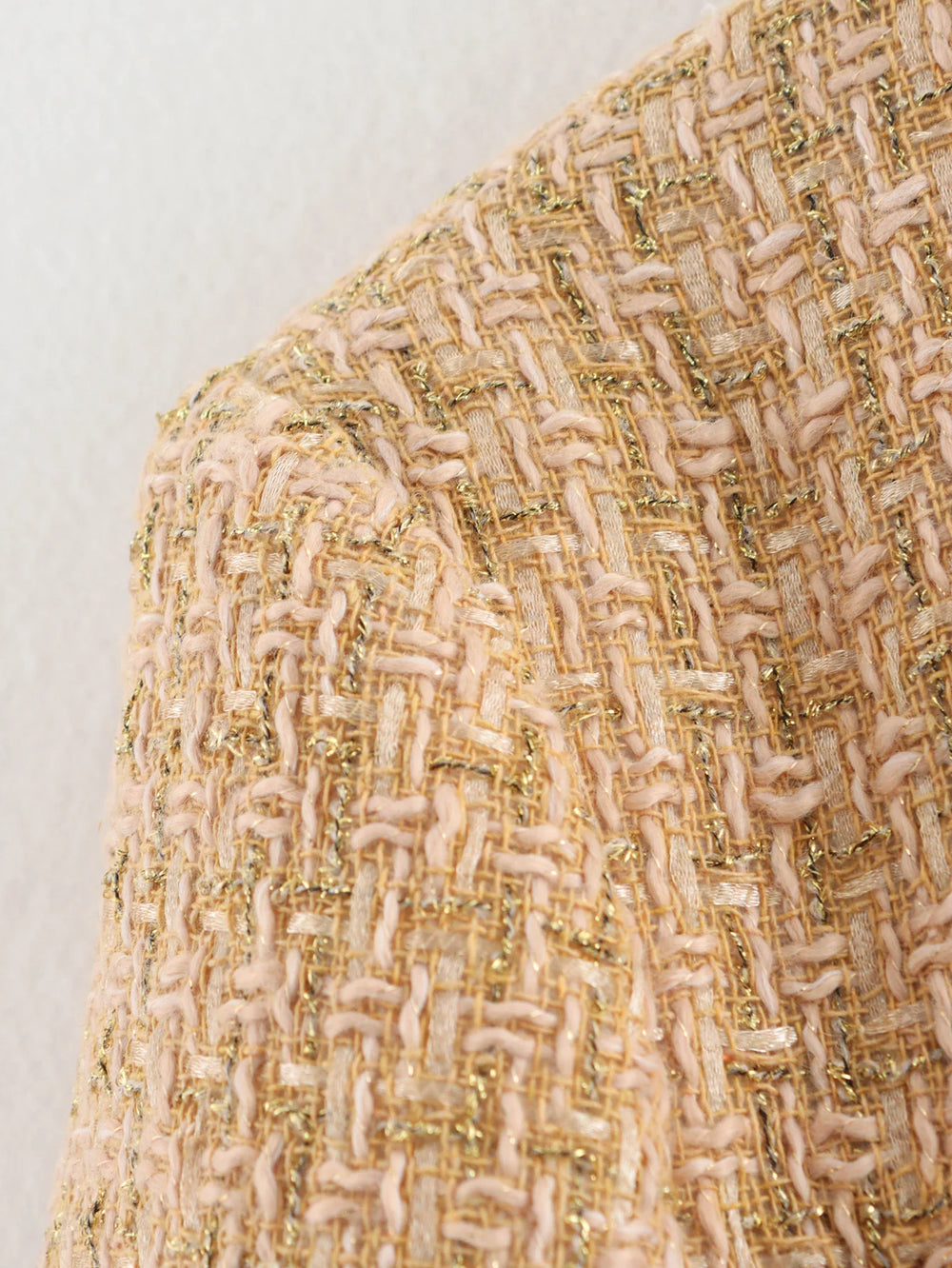 Close-up of a textured fabric with gold and beige pattern on a light gray background