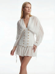 Woman wearing a white dress with long sleeves and gold buttons on a white background