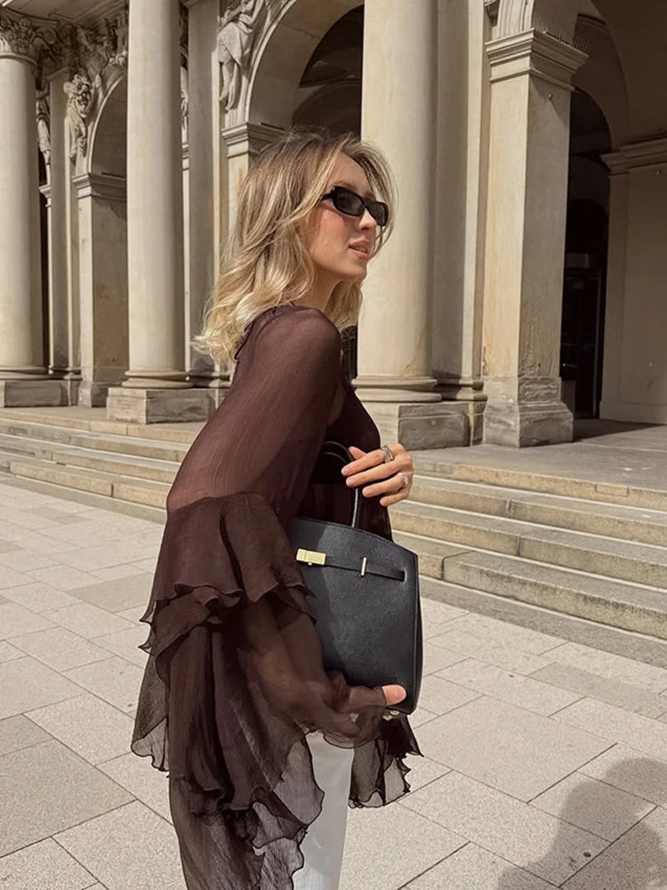 Woman in a brown dress holding a black handbag in front of classical architecture.