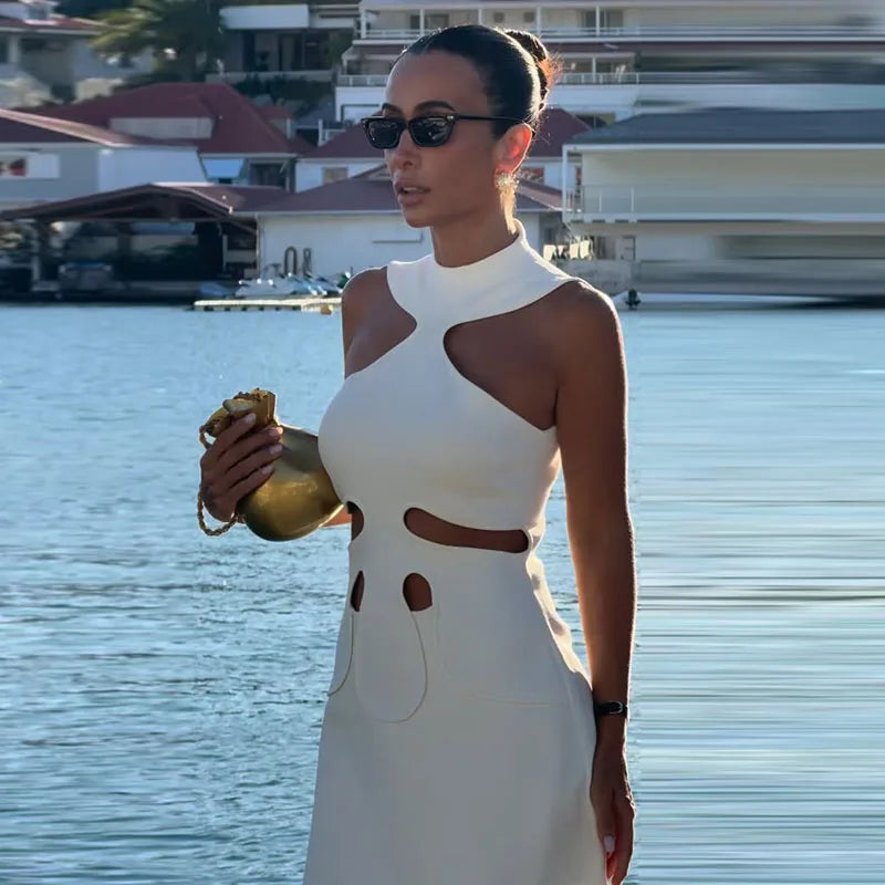 Woman in a white dress holding a gold clutch by a waterfront