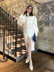 Woman in a white outfit standing on a staircase with patterned wall behind