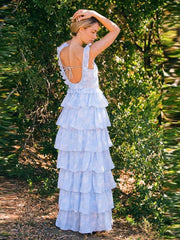Woman wearing a white tiered dress standing in a natural setting with greenery.