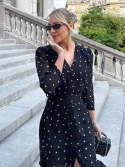 Woman in a black polka dot dress standing on stone steps with greenery in the background