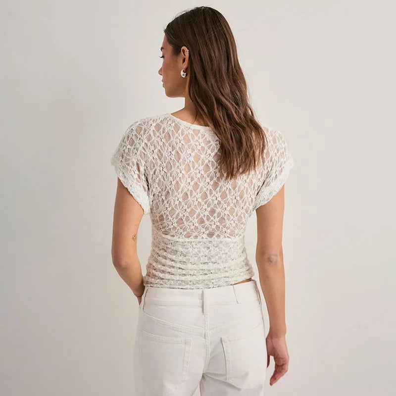 Woman wearing a white lace top and white pants against a plain background