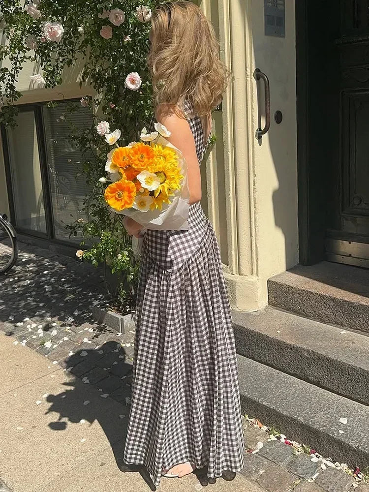 Woman in a checkered dress holding a bouquet of flowers outside a building.