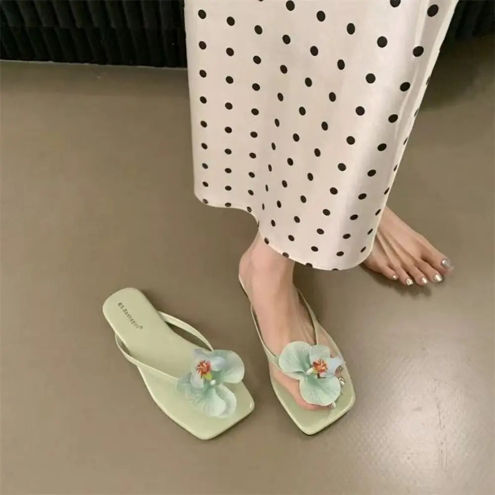 Light green sandals with floral decorations worn by a person in polka dot pants.