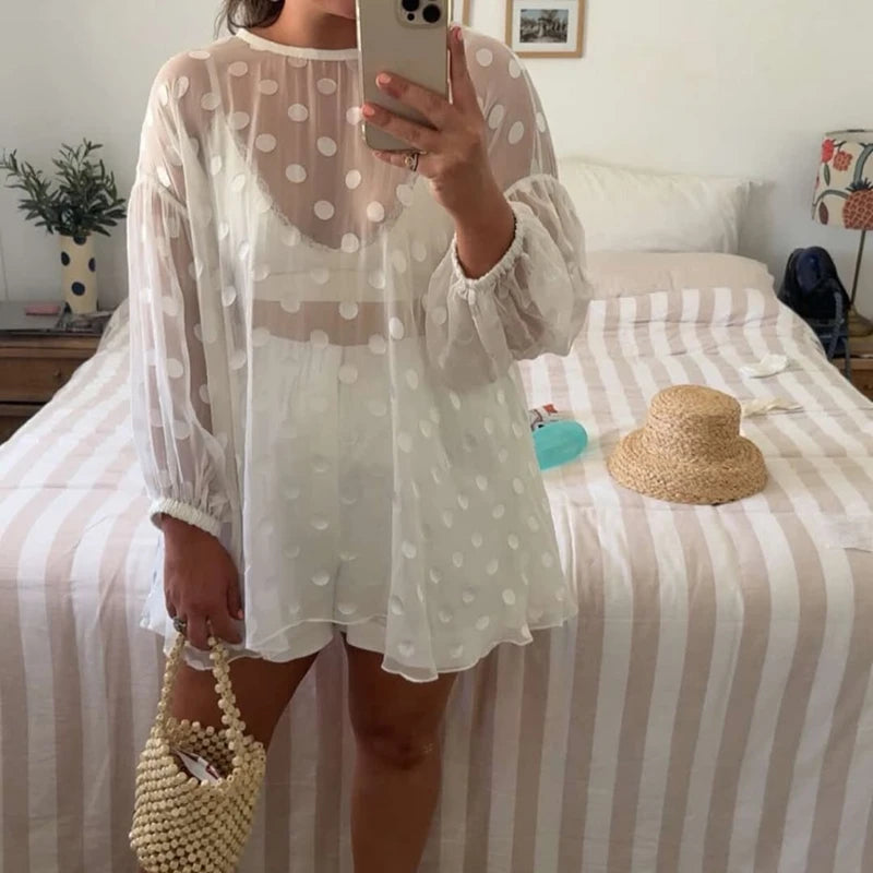 Person wearing a white polka dot dress taking a mirror selfie in a bedroom.
