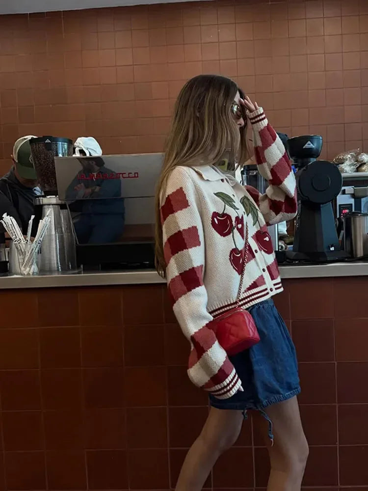 Person wearing a red and white sweater with cherry design in a coffee shop.