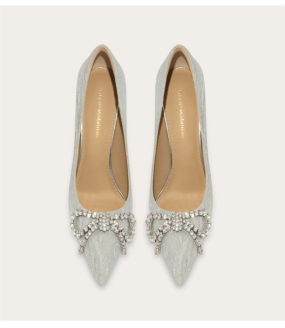 Pair of silver pointed-toe shoes with embellishments on a light gray background
