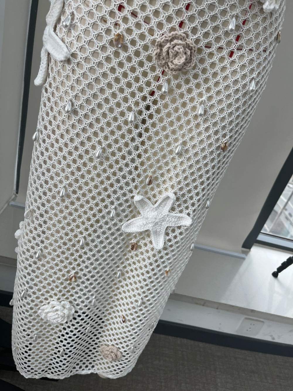 Decorative fishnet curtain with starfish and shell patterns in a room setting.