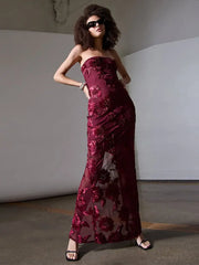 Woman wearing a burgundy strapless gown with floral patterns in a minimalistic setting.