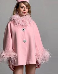 Woman wearing a pink coat with feather details and matching hat against a gray background
