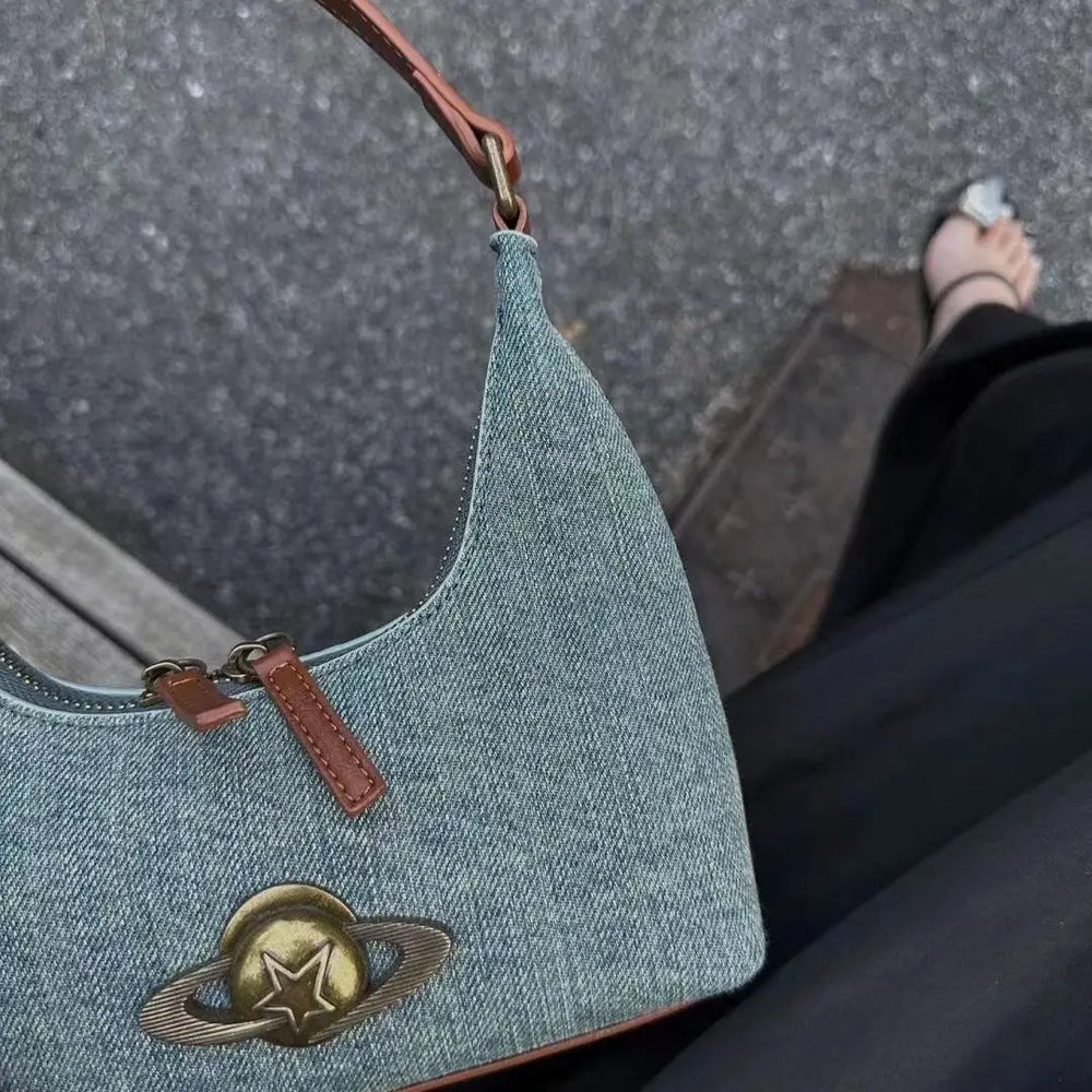 Denim handbag with a planet emblem on a blurred street background