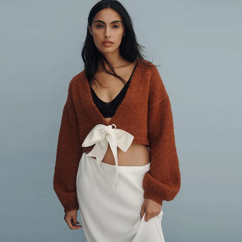 Woman wearing a brown cardigan over a black top and white skirt on a gray background