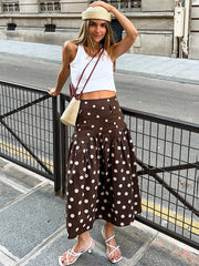 Woman in a white top and brown polka dot skirt standing on a city street.