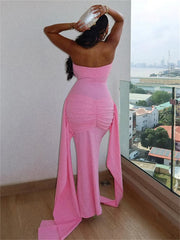 Woman in a pink strapless dress standing by a window with a cityscape view.