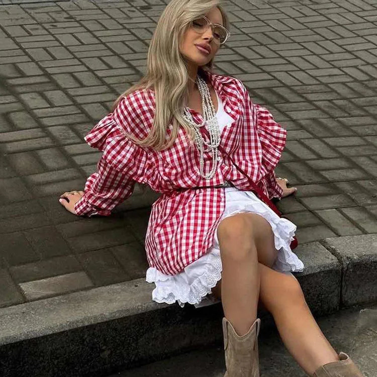 Woman in a red and white checkered shirt with ruffled sleeves sitting on a step.