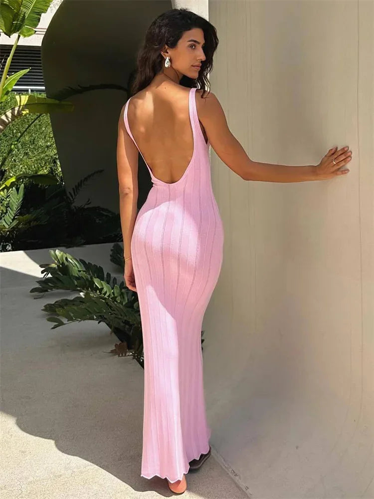 Woman in a pink evening gown with an open back, standing outdoors.