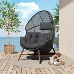 Black egg-shaped chair on a wooden deck with a scenic view of water and sky.
