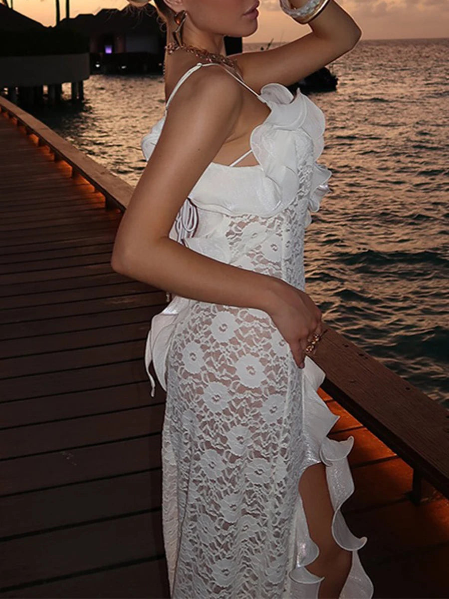 Woman in a white lace dress standing on a dock by the ocean at sunset.