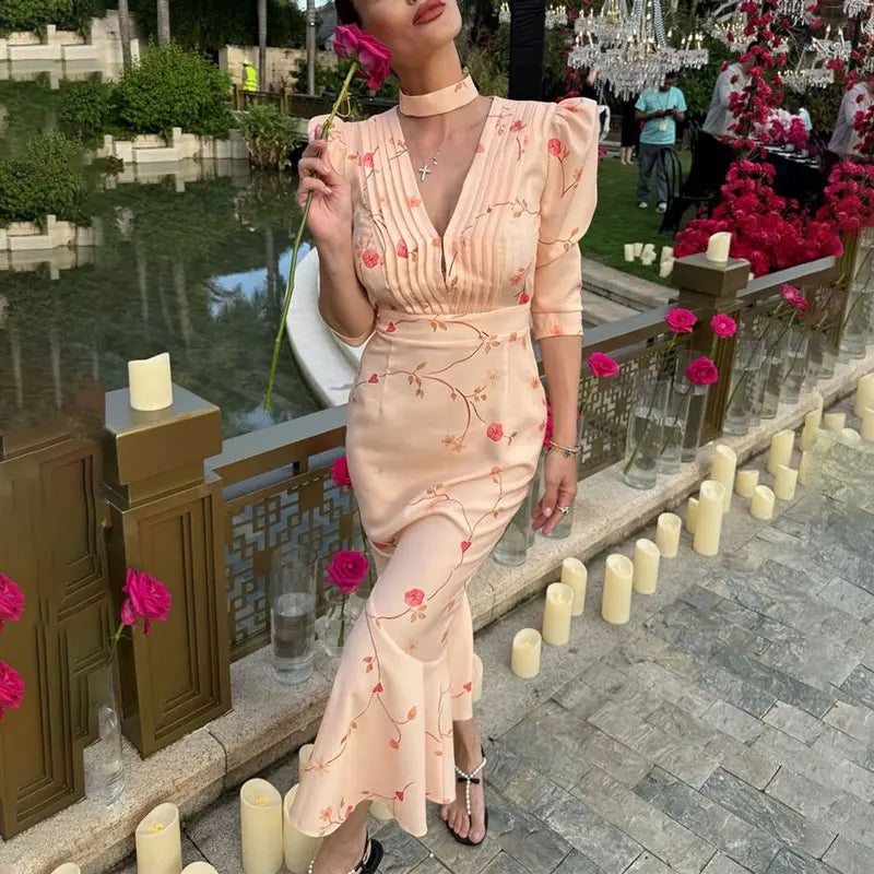 Woman in a floral dress standing outdoors with candles and flowers.