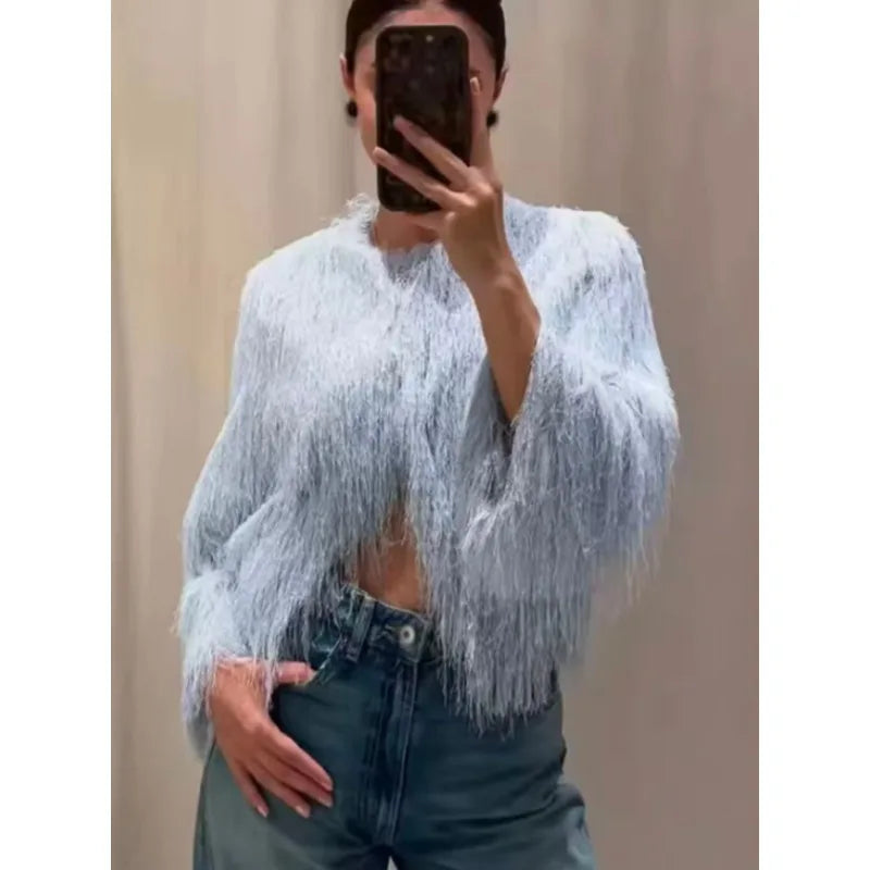 Person wearing a light blue fringed top and dark jeans against a plain background