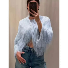 Person wearing a light blue fringed top and dark jeans against a plain background