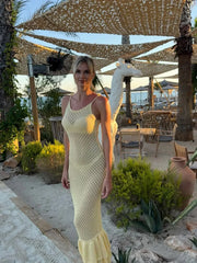 Woman in a yellow dress standing outdoors with palm trees and a beach setting.