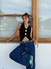Woman posing by a window wearing a black sleeveless top and blue jeans.