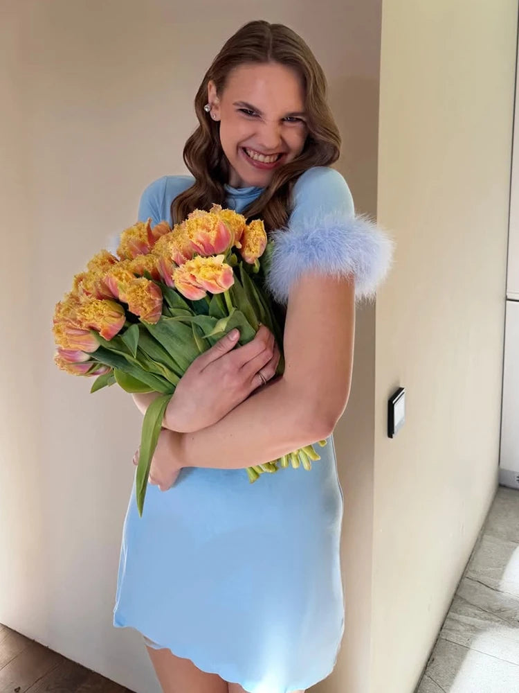Woman in a light blue dress holding a bouquet of flowers indoors.