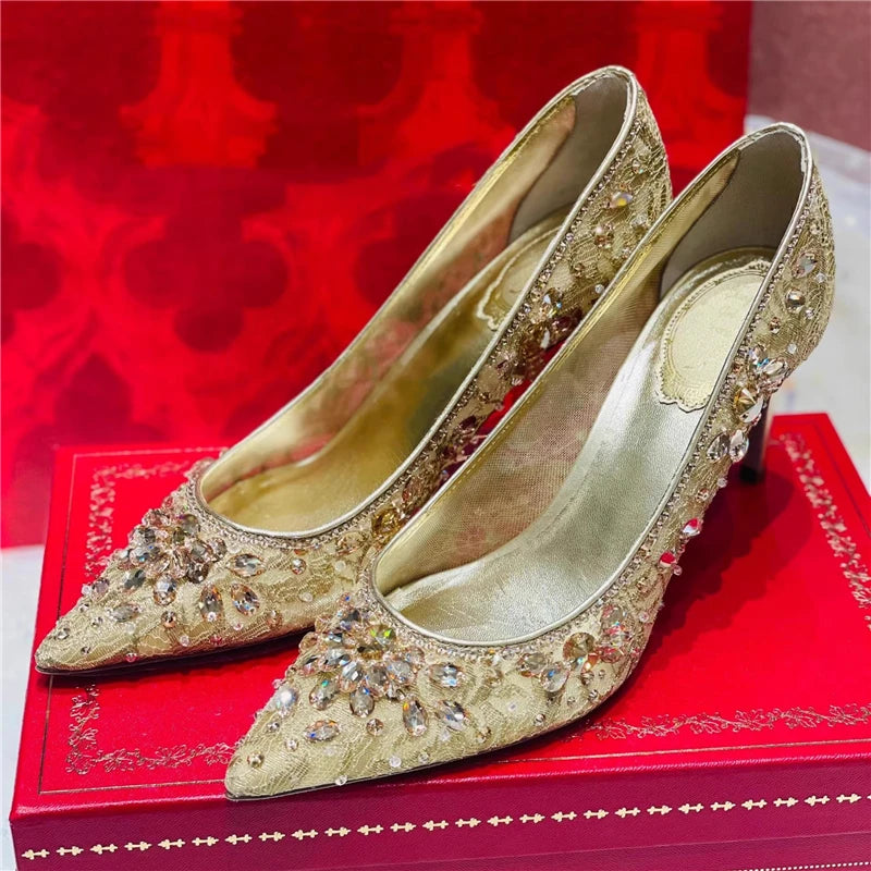 Gold high-heeled shoes with rhinestone embellishments on a red box.