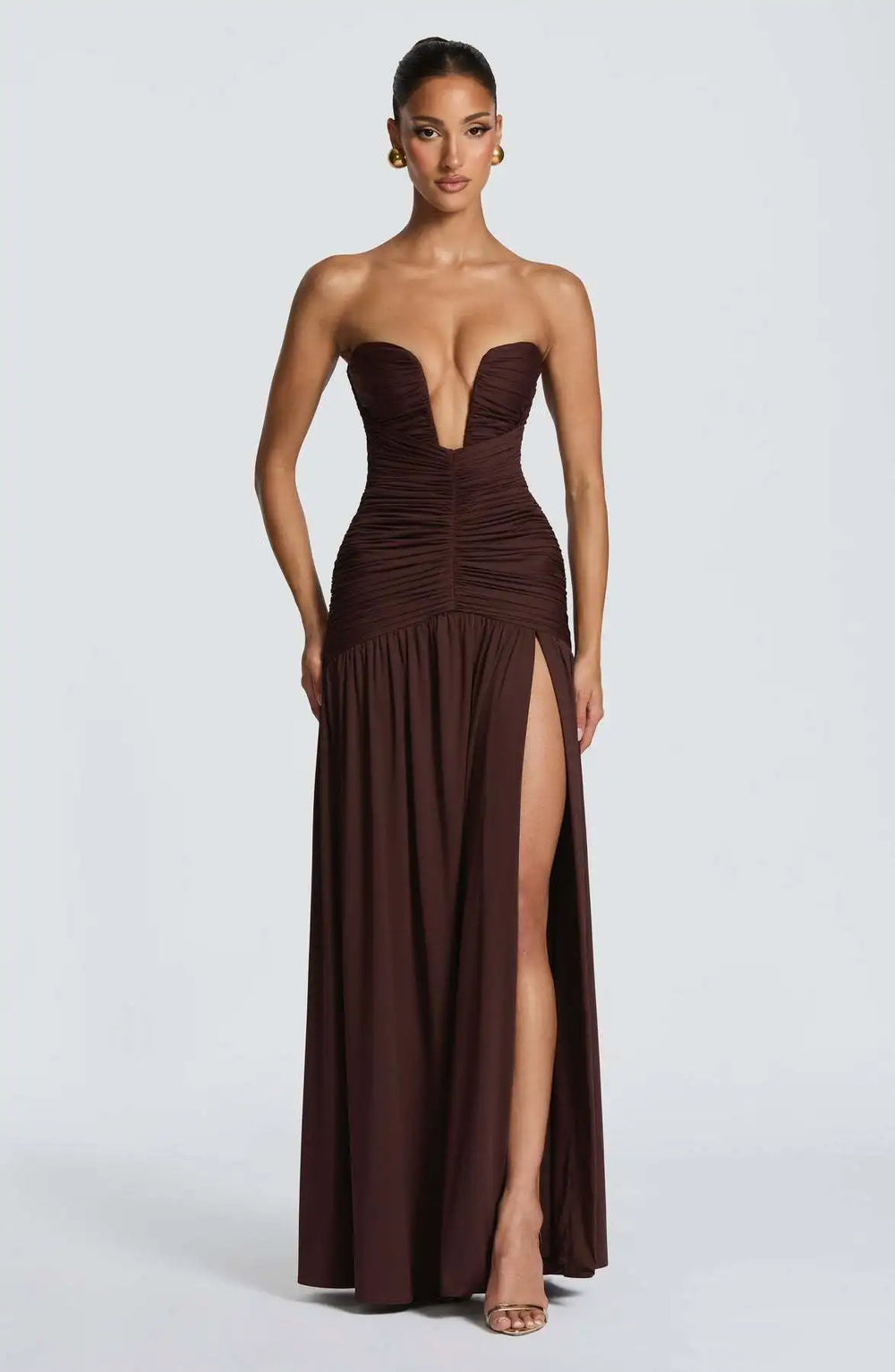 Woman wearing a strapless brown evening gown with a high slit on a white background