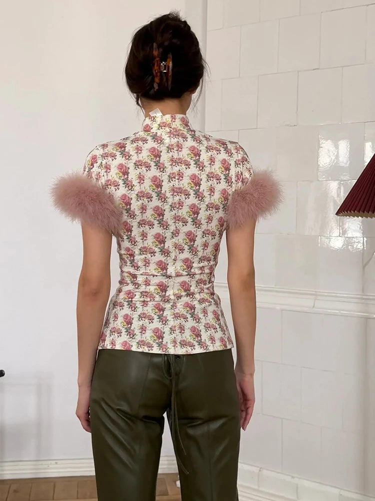 Person wearing a floral top with pink feather accents and green pants in a tiled room.