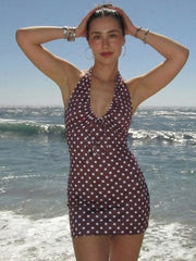 Woman in a polka dot dress standing on a beach with ocean waves in the background