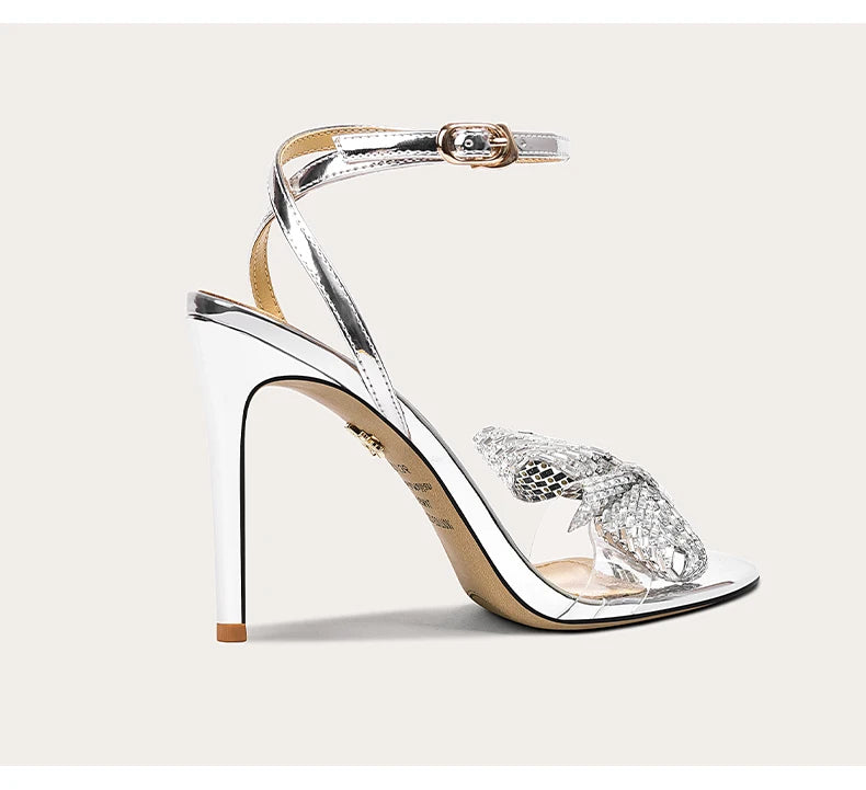 Silver high-heeled sandal with crystal embellishments on a light beige background