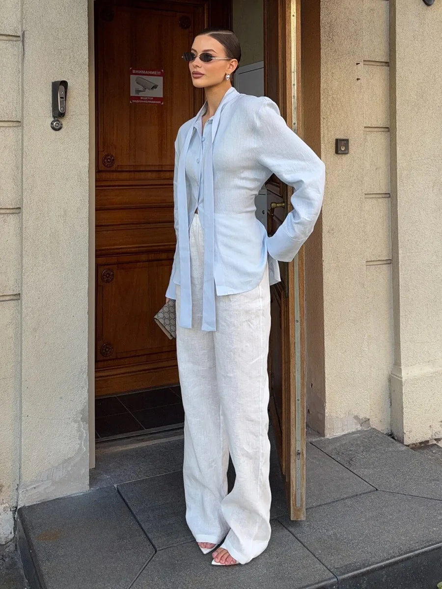 Woman in light blue shirt and white pants standing outside a building.