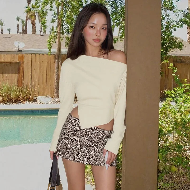 Woman in a light-colored top and patterned shorts standing by a pool with palm trees in the background.