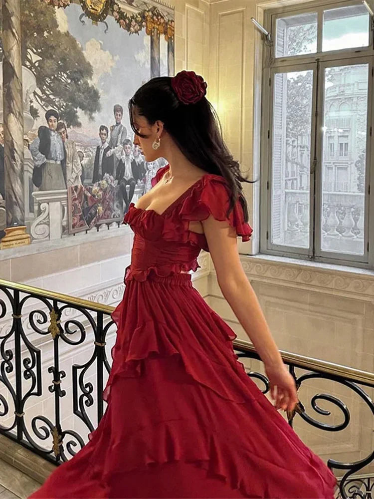 A woman posing in a flowing red dress with layered ruffles, accentuating the elegant silhouette.