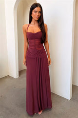 Woman wearing a burgundy evening gown standing against a white wall.