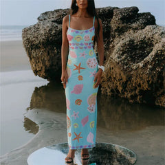 Woman in a floral dress standing on a beach with large rocks.