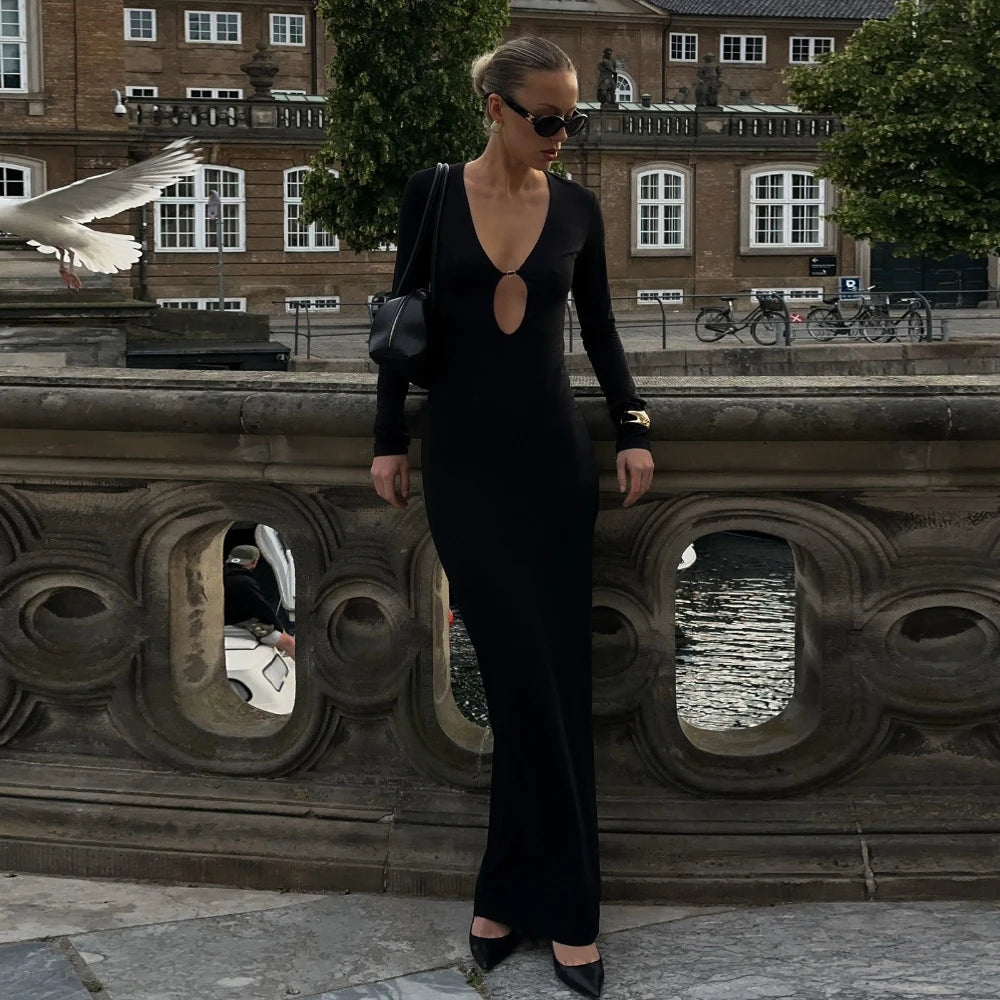Woman in a black dress standing on a stone bridge with a building and trees in the background.