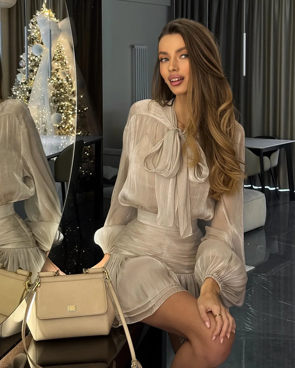 Woman in a light dress sitting in a room with a Christmas tree in the background