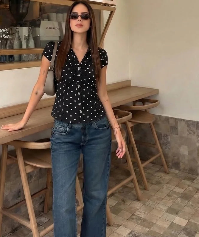 Woman in a polka dot shirt and jeans standing in a cafe.