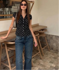 Woman in a polka dot shirt and jeans standing in a cafe.