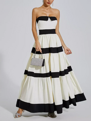 Woman wearing a black and white strapless dress with a clutch on a plain background