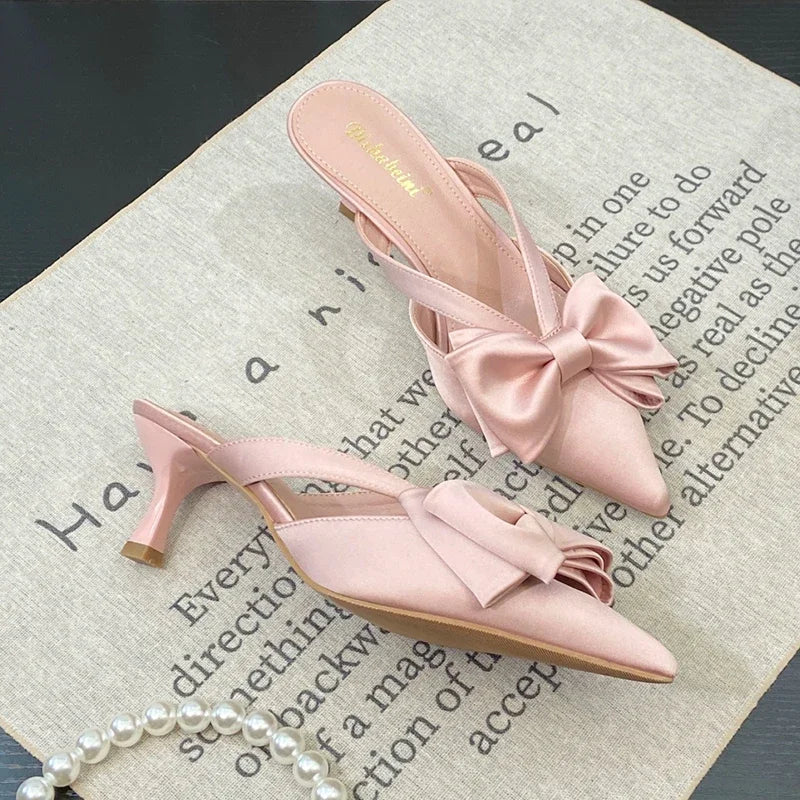 Pink high-heeled shoes with bow details on a textured surface